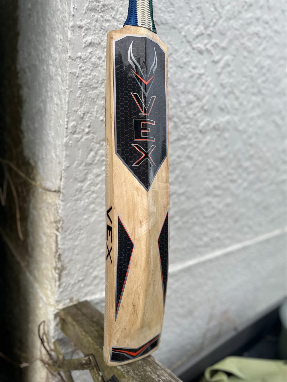 Cricket bat blade with black honeycomb VEX stickers in orange and silver-grey, and VEX lettering on the edge
